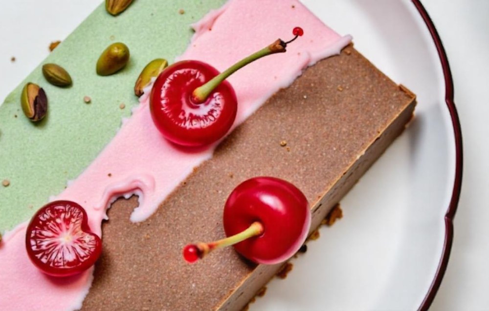 Close-up of spumoni ice cream with vibrant green, red, and brown layers, topped with whipped cream and a cherry.