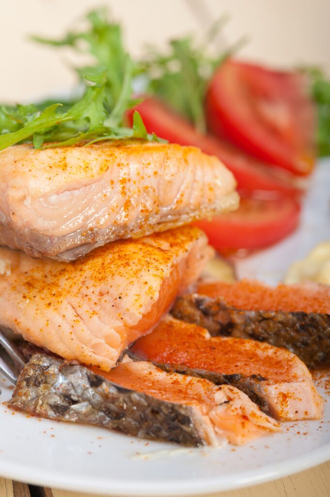 A perfectly cooked pink salmon fillet served with roasted vegetables and garnished with fresh herbs.