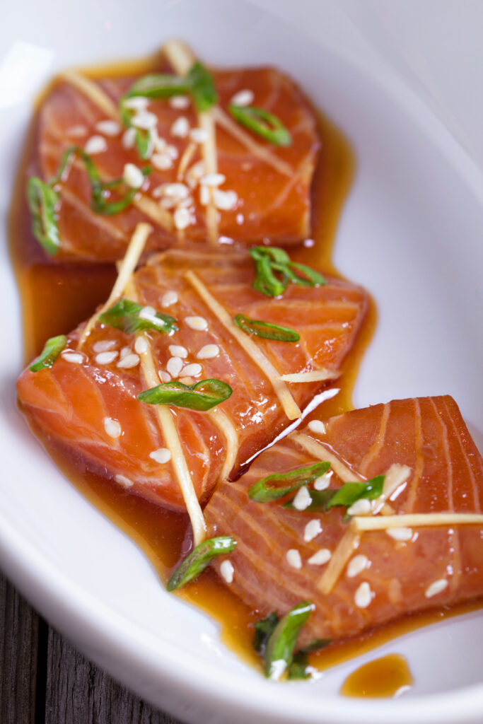 Freshly sliced salmon sashimi served on a plate with garnishes of daikon radish and soy sauce