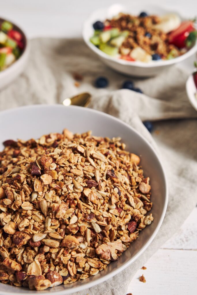 A bowl of homemade protein granola with oats, nuts, and seeds, served with fresh berries and yogurt on a rustic wooden table.