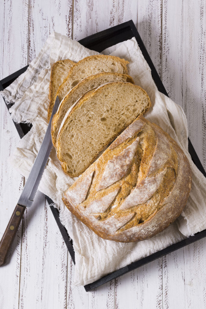 A rustic loaf of artisan Italian bread placed next to a slice of plain white bread, showcasing their differences in texture and appearance.