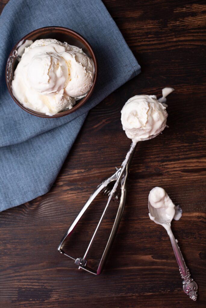 A stainless steel ice cream scoop with an ergonomic handle, perfectly scooping a round ball of vanilla ice cream.