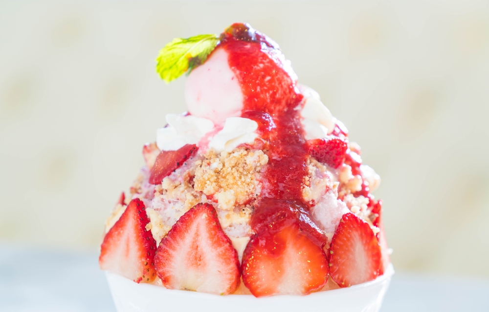 Close-up of strawberry shortcake ice cream in a waffle cone, showcasing swirls of strawberry sauce, chunks of buttery shortcake, and a sprinkle of powdered sugar.