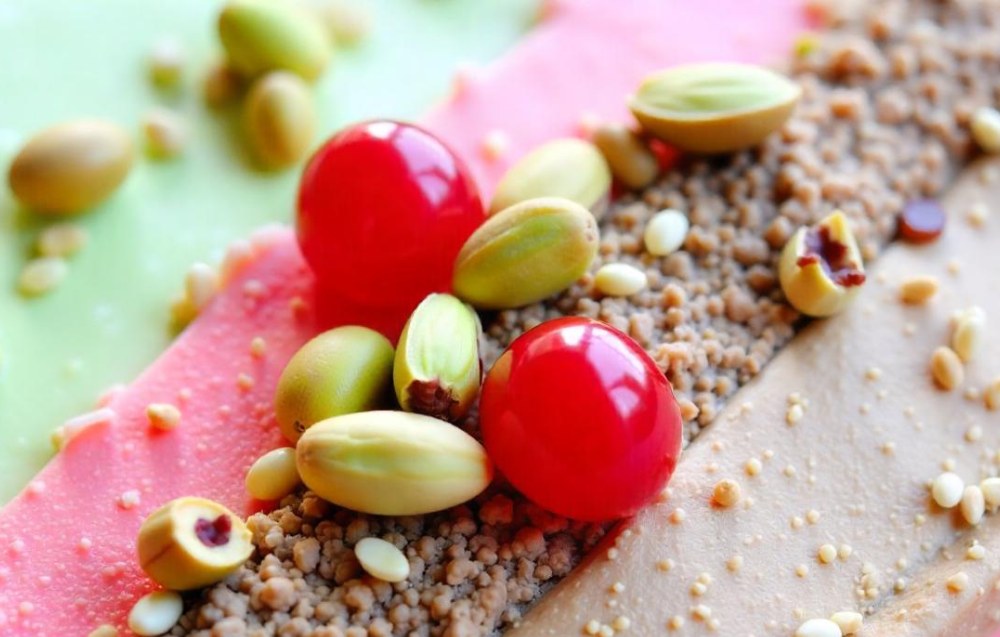 A colorful slice of spumoni ice cream showing layers of pistachio, cherry, and chocolate with nuts and fruits mixed in.
